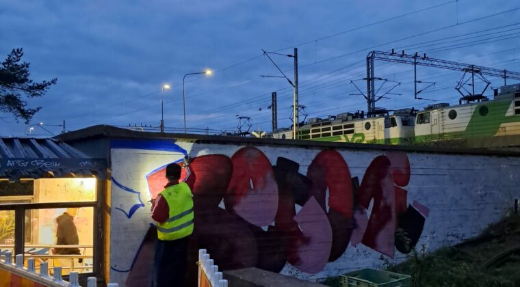 Henkilö maalaa luvallista graffitia seinään. Aurinko laskee, hämärtää.