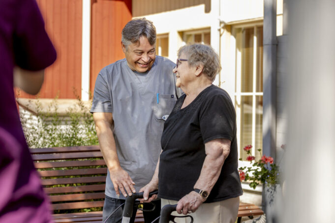 Hoitaja auttaa vanhusta, joka käyttää rollaattoria.