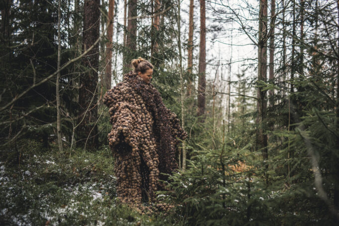 Nainen metsässä päällään männynkävyistä tehty palttoo.