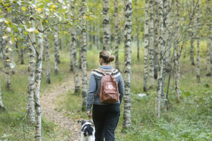 Kuvassa nainen kävelee luontopolulla koiransa kanssa.